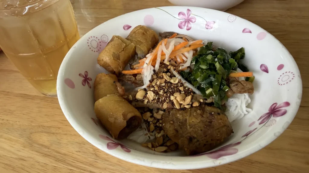 Hoàng Vănのブンティットヌン。米麺の上に焼き豚、揚げ春巻き、なます、ネギ油、ピーナッツとごまがのっている
